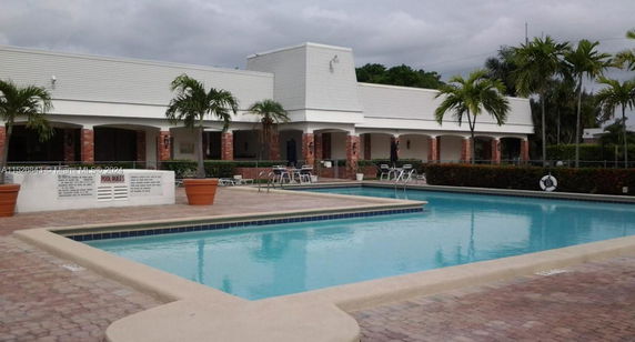 Outdoor swimming pool with surrounding patio and building with arches.