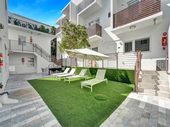 Outdoor area of a building with lounge chairs and umbrellas on artificial turf.