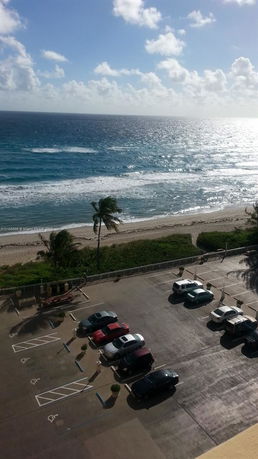 View of the ocean and beach from a higher elevation, overlooking a parking lot.