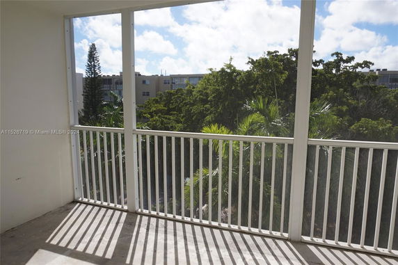 View from a balcony with white railing overlooking trees and a building in the distance.