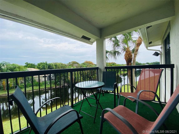 A balcony with chairs and a table overlooking a scenic outdoor area with trees and a water body.