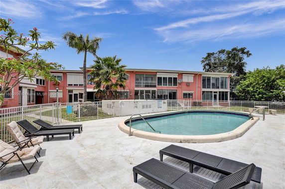 Outdoor swimming pool area with lounge chairs in front of a two-story building.
