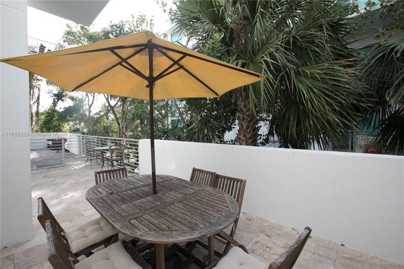 Outdoor patio area with a wooden table, chairs, and a large yellow umbrella.