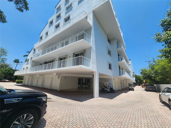 Outdoor parking area beneath a multi-story building with balconies.