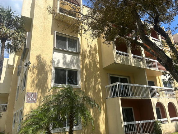 Front view of a multi-story residential building with balconies and tall trees in front.
