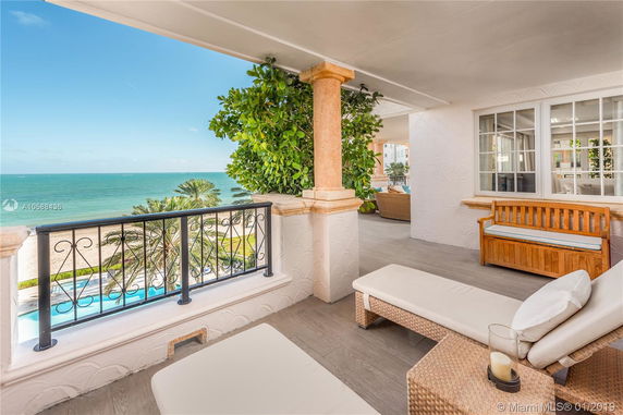 Balcony view overlooking a beach and ocean, with outdoor seating and decorative plants.