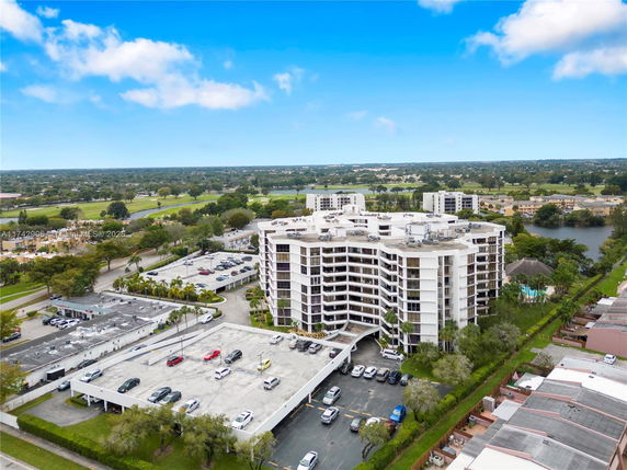 Aerial view of a multi-story apartment building surrounded by parking areas and greenery.