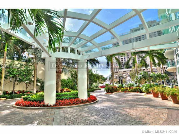 Outdoor area with a glass canopy and landscaped surroundings near a building entrance.