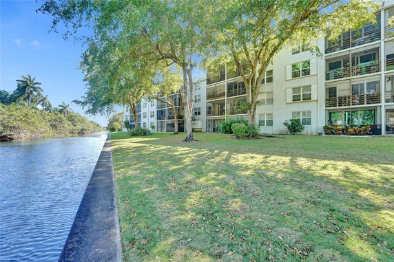 View of a multi-story apartment building with balconies next to a waterway and surrounded by trees.