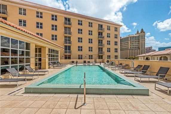 Outdoor swimming pool with lounge chairs beside a multi-story building.