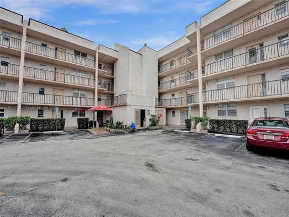 Front view of a multi-story apartment building with balconies and a parking area.