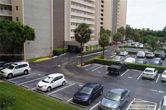 View of a multi-story building with adjacent parking lot and palm trees.