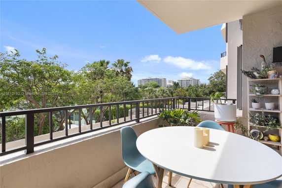 Outdoor balcony area with chairs and table overlooking surrounding greenery and buildings.