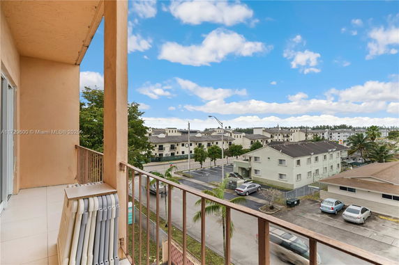 View from a balcony overlooking residential buildings and a parking area.