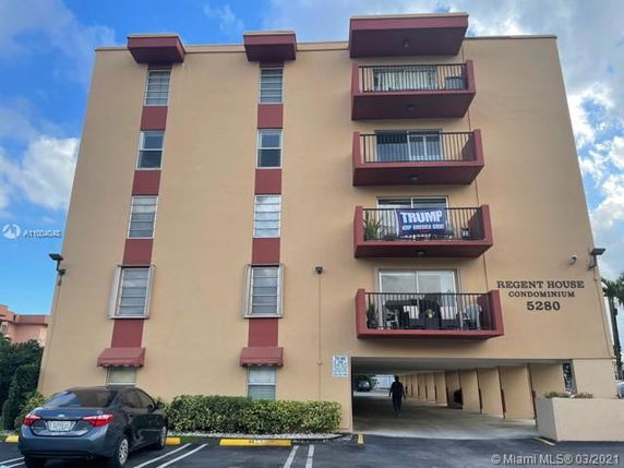 Front view of a multi-story condominium building with balconies and a parking area below.