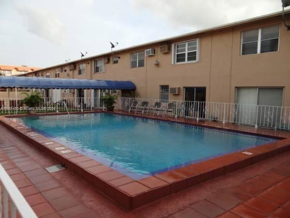 Swimming pool adjacent to a two-story building with a fenced perimeter.