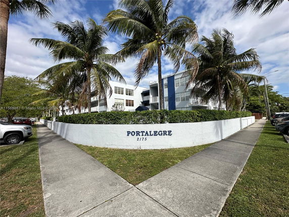 Front view of a multi-story building with palm trees and a low surrounding wall.