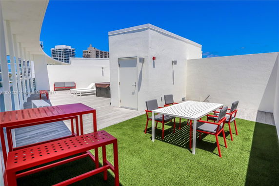 Rooftop patio with modern furniture including tables and chairs, surrounded by white walls and featuring artificial grass flooring.