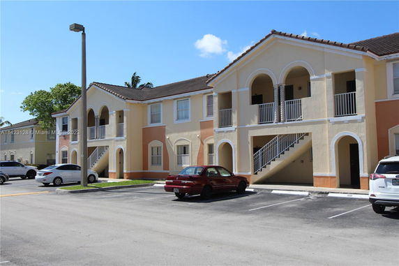 Front view of a two-story building with arched balconies and a parking area.