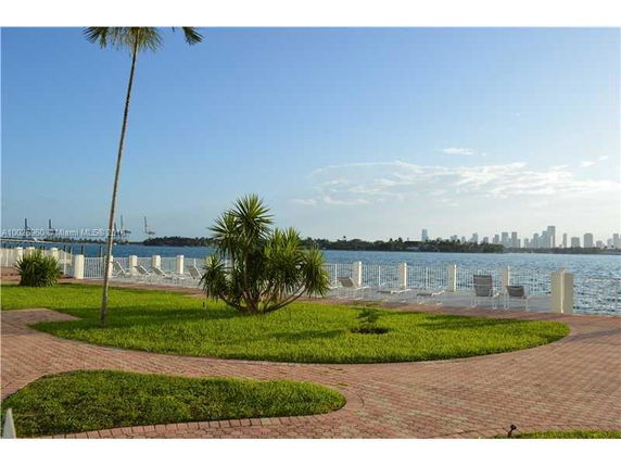 View of waterfront area with chairs, grass, and city skyline in the background.