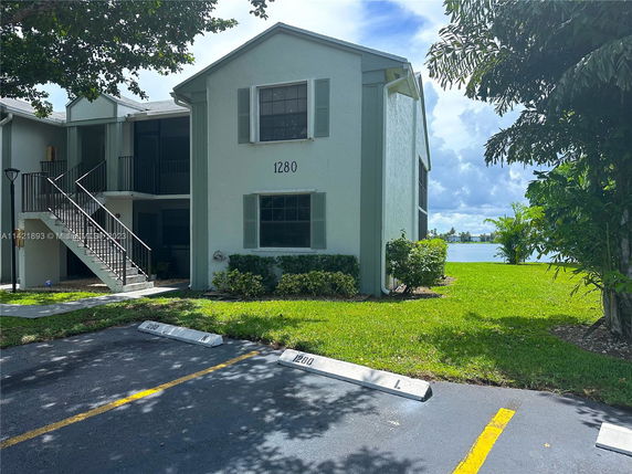 Front view of a two-story building with a staircase leading to the entrance and a lake view in the background.