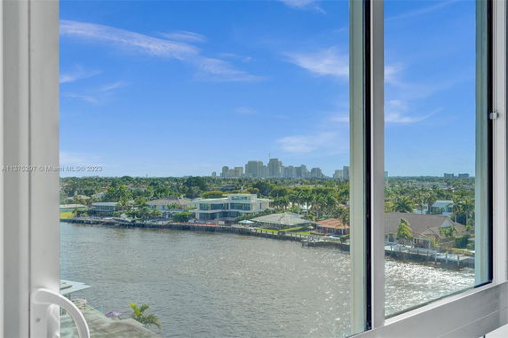 View of a waterfront area with several houses, palm trees, and a city skyline in the distance seen from a building window.
