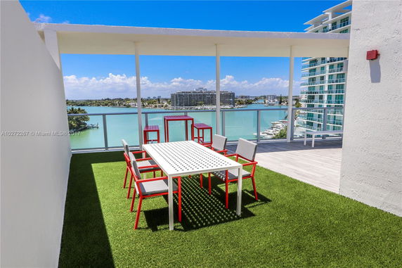 Rooftop area with a table and chairs overlooking a body of water and distant buildings.