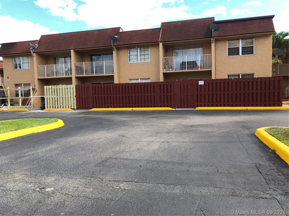 Front view of a multi-story residential building with balconies and a parking area.