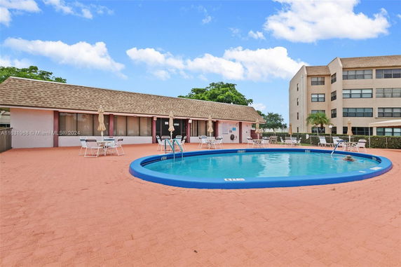 View of an outdoor swimming pool with lounging chairs and umbrellas around it, adjacent to a building.