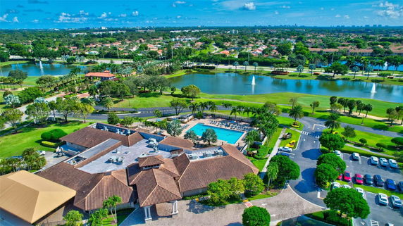 Aerial view of a residential area with a clubhouse, swimming pool, and landscaped gardens next to a lake.