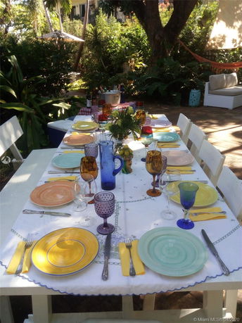Outdoor dining area with a table set with colorful plates and glasses, surrounded by lush greenery.