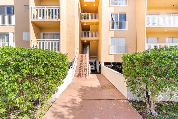 Front view of an apartment building with balconies and a parking area underneath.