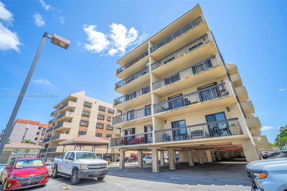 Front view of a multi-story apartment building with balconies and covered parking area.