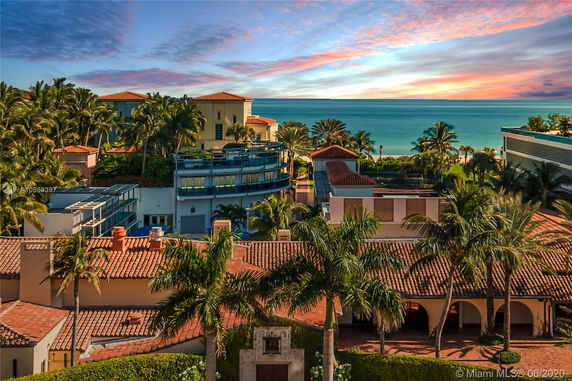 View of a coastal area with multiple buildings, palm trees, and a beach in the background.