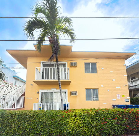 Front view of a two-story building with balconies and a palm tree.