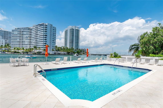 Outdoor swimming pool with lounge chairs and nearby modern high-rise buildings.