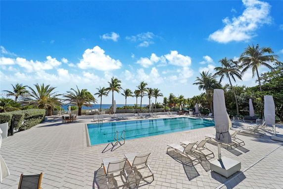 Outdoor swimming pool area with loungers and palm trees.