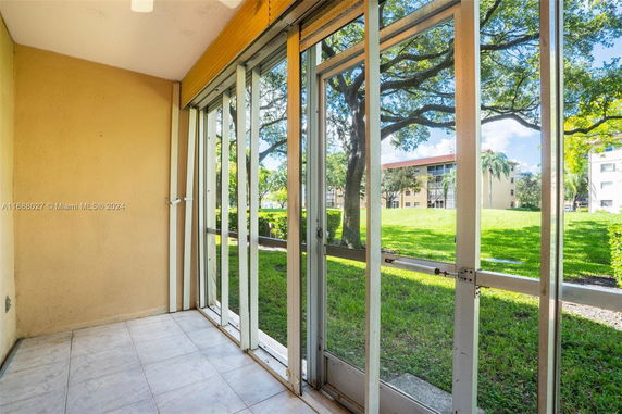 View of grassy area with trees and surrounding buildings from a glass-enclosed patio.