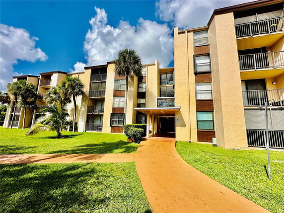 Front view of a multi-story apartment building with balconies and entrance pathway.