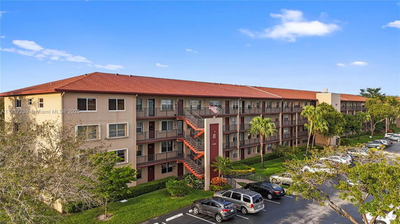 Front view of a multi-story apartment building with exterior staircases and parking area.
