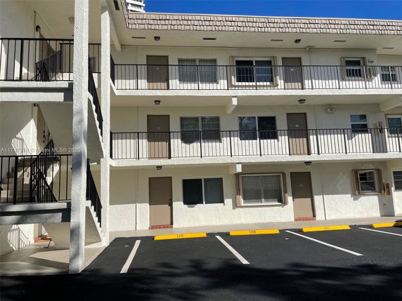 Front view of a multi-story building with external staircases and parking spaces.