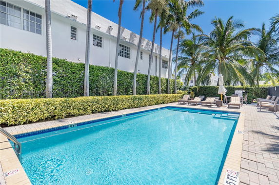 Outdoor swimming pool area with lounge chairs and palm trees.