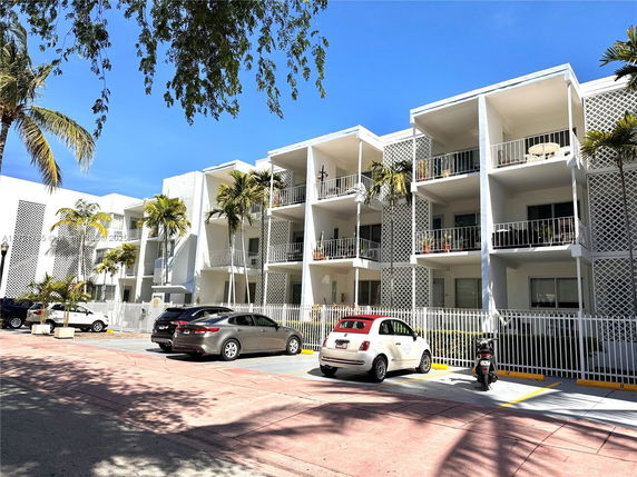 Front view of a three-story apartment building with balconies and a parking area in front.
