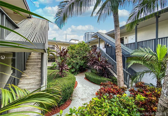 View of a small garden area surrounded by two-story building walkways with tropical plants.