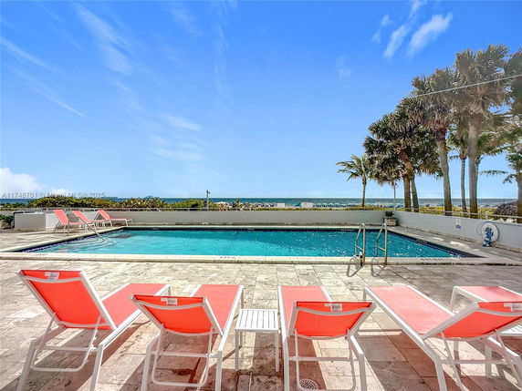 Outdoor swimming pool area with lounge chairs and ocean view.
