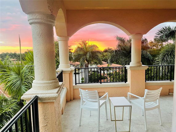 Outdoor balcony view with chairs and palm trees at sunset.