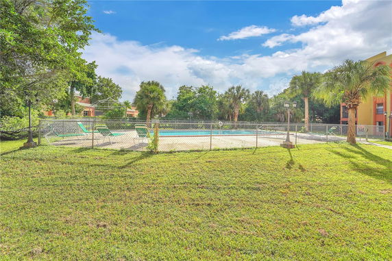 Outdoor swimming pool surrounded by a fence with palm trees nearby.
