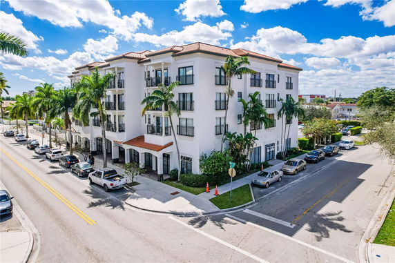Front view of a multi-story building with palm trees and parked cars.