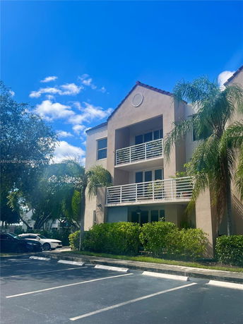 Front view of a multi-story building with balconies and a parking area.