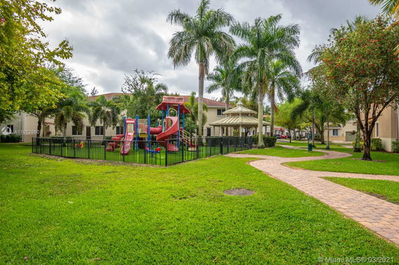 Playground with slides and climbing structures surrounded by a fence in a landscaped area.
